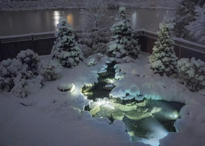 A wintery koi pond with outdoor lighting.